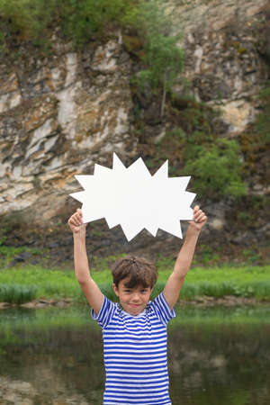 Little boy standing on bank of river keeping blank white board in hands above his head. Your text here.の写真素材