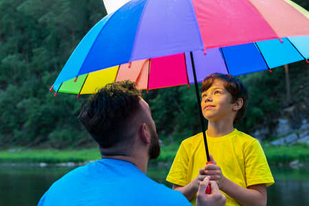Bearded man and his teen sun under umbrella look up. boys face lit.の写真素材