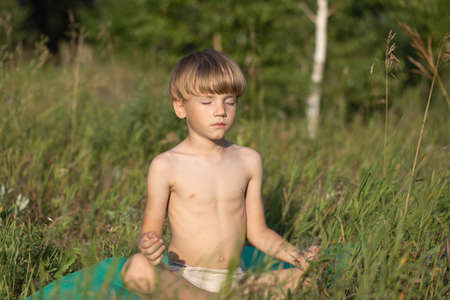 boy meditating during yoga class outside in park in summer timeの写真素材