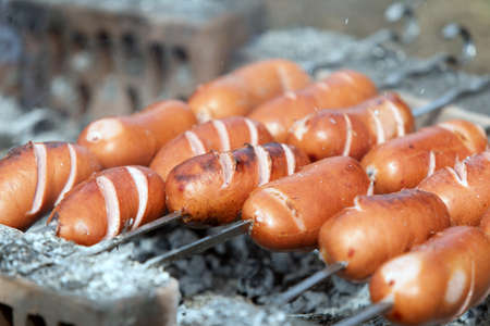 Sausages are grilled on skewers on fire, smoke is visible. Close upの写真素材