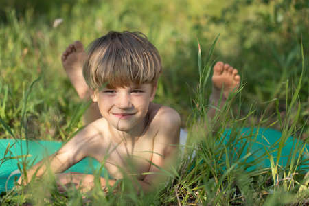 young kid boy lies on green grass in sunny countrysideの写真素材