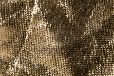 rough gold surface with sun glare as background. crumpled texture of smooth material patterned...