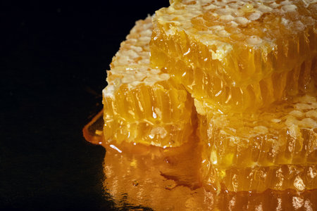 Golden pieces of fresh honeycomb with drops of honey on blurry dark backgroundの写真素材
