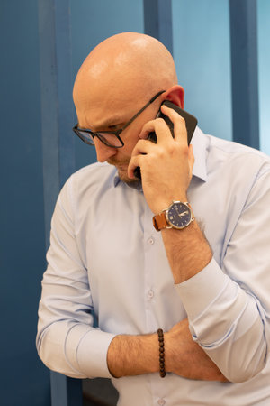 bald man with glasses with worried look calls on mobile phone businessman solves problems