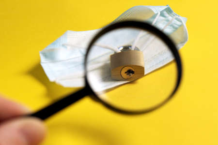 search for opportunity to remove lockdown. end of World isolation of coronavirus pandemic. medical mask closed with lock, keyhole through magnifying glassの写真素材