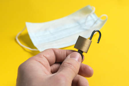 end of World isolation of pandemic. world is open after coronavirus quarantine. open lock with key in hand on background of medical mask.の写真素材