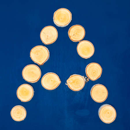 Handmade letter A of sawn birch wooden logs on round discs on blue back