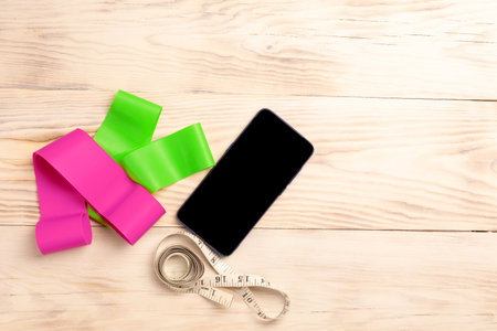 Smartphone, elastic bands for fitness, measuring tape on wooden background. Concept of healthy...