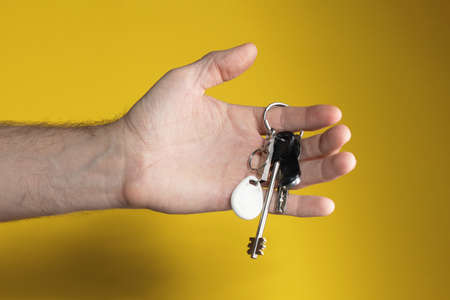 Hand holding key chain on yellow background. Building concept