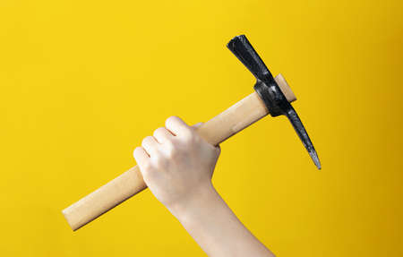 Close-up of pickaxe in man hand on yellow background. Advertising of tools for construction or dismantling. Poster for shop or necessary item for mountain climber or for finding precious stones.の写真素材