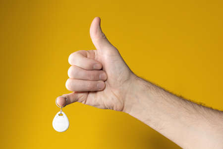 Man hand in form of raised thumb with hanging drop-shaped steel tag on little finger on yellow brown background. Successful in case. Everything is OK. Got what wanted.の写真素材