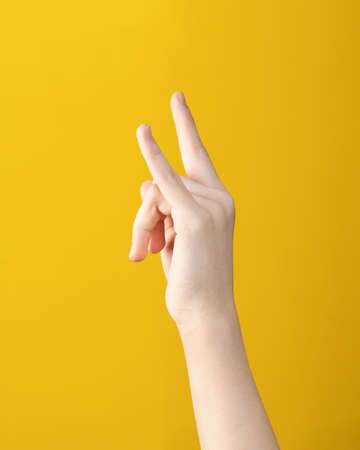teen hand with two fingers up shows goat gesture on yellow background. symbol of heavy metal and...