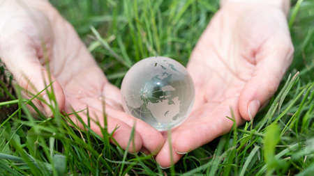 environment concept. Close up of glass globe in hand on nature background with copy spaceの写真素材