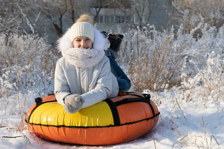 Teen girl riding snow tube on sunny winter day. Funny family games on winter vacation.