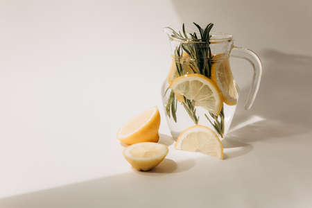 Refreshing lemonade with rosemary in a glass jug on a light beige background. Front viewの写真素材