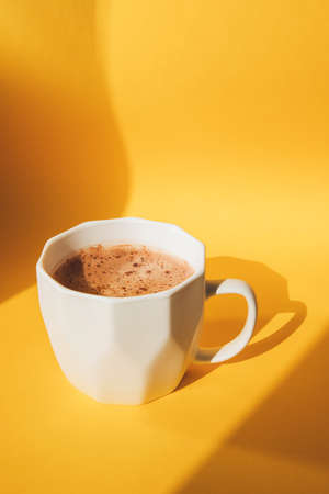White cup with cocoa on a yellow background with shadows. Front viewの写真素材