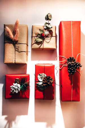 Red and brown gifts decorated with dried flowers and pine cones on a light background. Christmas bustle. Flat layの写真素材