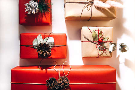 Red and brown gifts decorated with dried flowers and pine cones on a light background. Christmas bustle. Flat layの写真素材