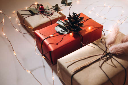 Red and beige gifts are decorated with dried flowers and pine cones on a light background with...