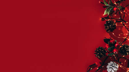 Christmas banner on a red background. Composition of Christmas lights, pine cones and decorative...