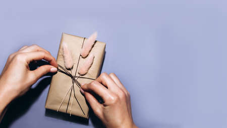 Banner, gift wrapping image on a lilac background. Girls hands tie a rope on a gift. Flat layの写真素材