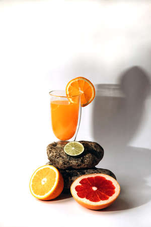 A glass of citrus juice on a podium made of stones. Image of juice with cut grapefruit, lime and orange lying on the table. Front viewの写真素材