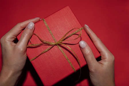 Red gift in the hands of a girl on a red background. Close-up