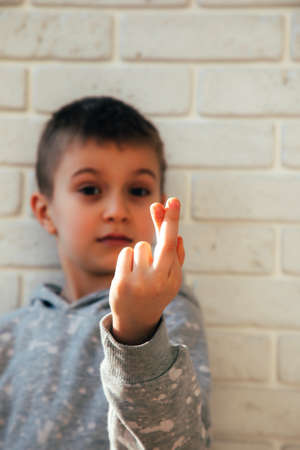 The boy smiles and shows a heart with his fingers. Portrait of a child against a white brick wall. Close upの写真素材