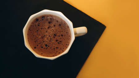 White cup of coffee with foam on a black and yellow background. Banner, top viewの写真素材