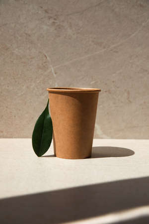 Zero waste concept. Paper glass on a stone beige background with a green leaf. Front viewの写真素材