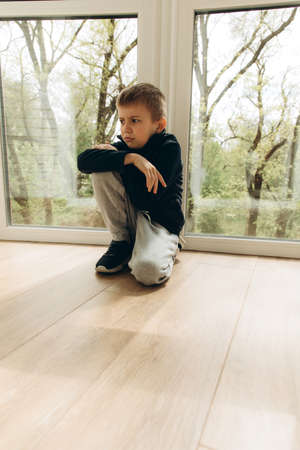 Upset, angry boy of 6-7 years old sits near the window. Portrait of a boy, front viewの写真素材