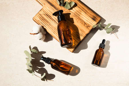 Clear bottles with organic cosmetics on a beige stone background with wooden plank. Flat layの写真素材