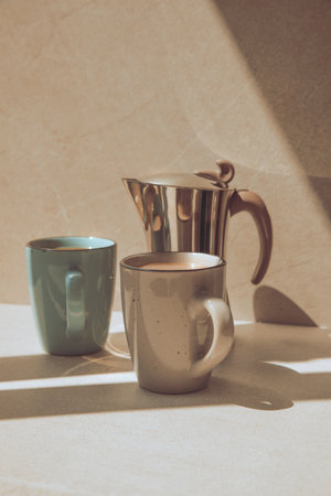 Two cups of coffee and a steel geyser coffee maker on a beige stone background. Front viewの写真素材