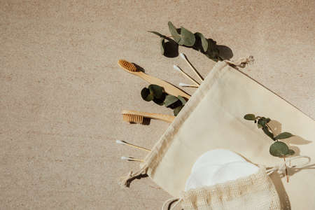 Two wooden toothbrushes, cotton pads and sticks and a wooden hairbrush on a light background with eucalyptus branches. Flat layの写真素材
