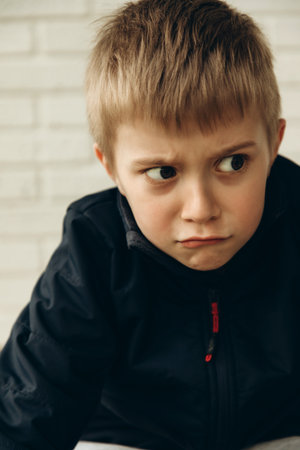 A pensive boy of 6-7 years old sits on the floor with a mysterious, cunning look. Portrait of a boy, front viewの写真素材