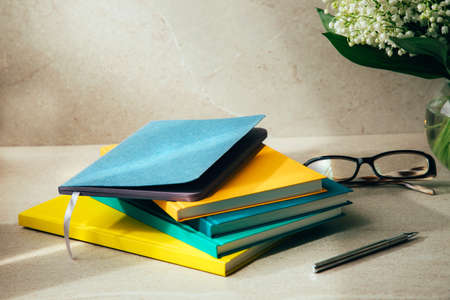 Multi-colored office notebooks and bouquet of lilies of the valley on a beige table with a pen....