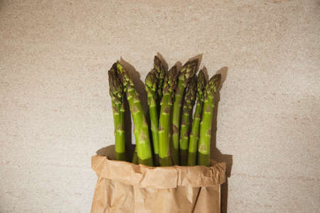Ripe fresh asparagus in a paper bag on a beige table, front viewの写真素材
