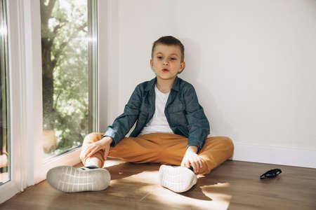 Joyful boy 6-7 years old in a blue shirt and yellow trousers sitting on the floorの写真素材