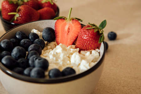 Curd with fresh blueberries and strawberries in a plate on a beige background. Healthy breakfast, front view, close upの写真素材