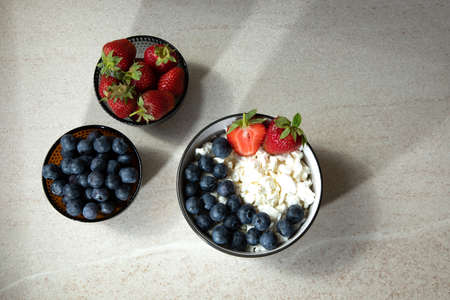 Curd with fresh blueberries and strawberries in a plate and bowls with fruits on a light background. Healthy breakfastの写真素材