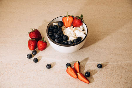 Curd with fresh blueberries and strawberries in a plate on a beige background. Healthy breakfastの写真素材