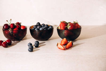 Fruits, blueberries, strawberries, cherries, in round glass plates on a beige table. Front viewの写真素材
