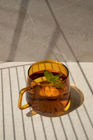 Mint tea in an orange glass mug on a light stone table with shadow stripes. Front viewの写真素材