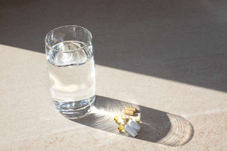Complex of organic bio supplements, vitamin d, calcium, omega on a beige stone table and a glass of...