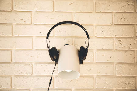 Black headphones are worn on a white lamp against the background of a white brick wall. Front viewの写真素材