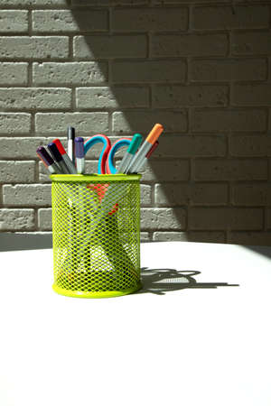 White office table with office supplies, colored pencils in green glass. Front view