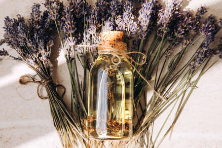 Close-up of lavender oil lying on lavender flowers on a light stone background. Top viewの写真素材
