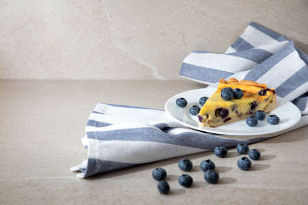 A piece of blueberry cheesecake on a white plate on a white striped tea towel. Front viewの写真素材