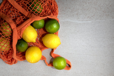 Orange mesh eco bag with fresh lemons and limes. Top view, copy spaceの写真素材