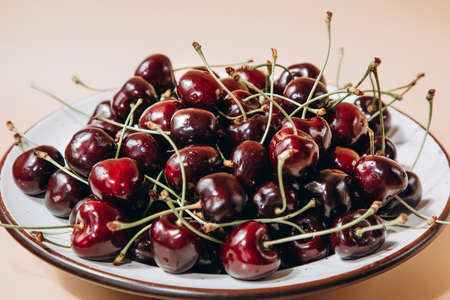 A large cherry close up in a white deep plate on a light orange background in sunlight, selective focus. Front viewの写真素材